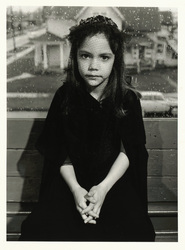 Photograph called Stacey, age 8, posing as Gertrude Stein, Bellingham, Washington, 1975 shows an 8 year old girl seated in front of a rain-drop spattered window wearing a black dress and black hat with her arms folded in front of her.